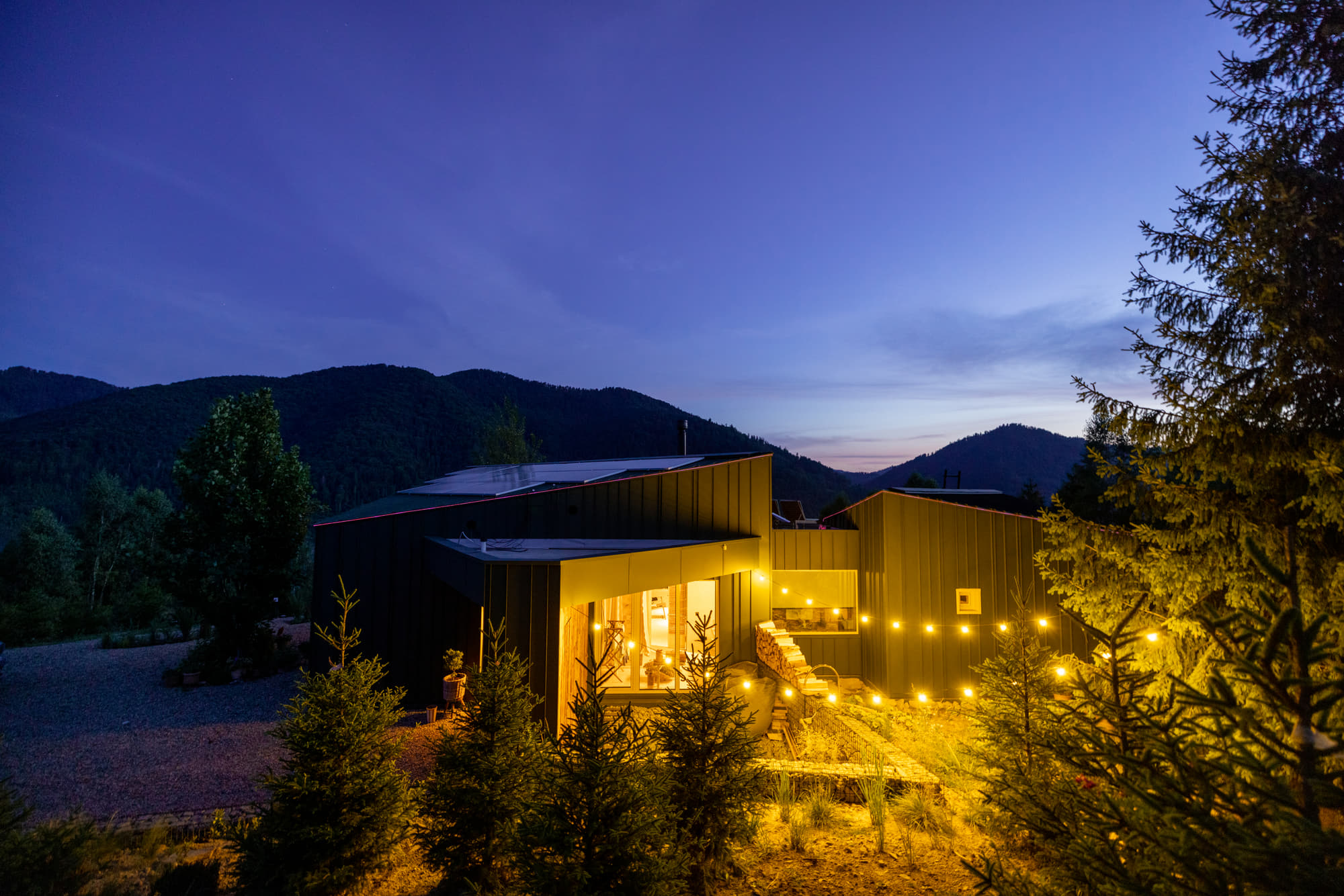 Modern home in the hills at dusk, windows glowing warm