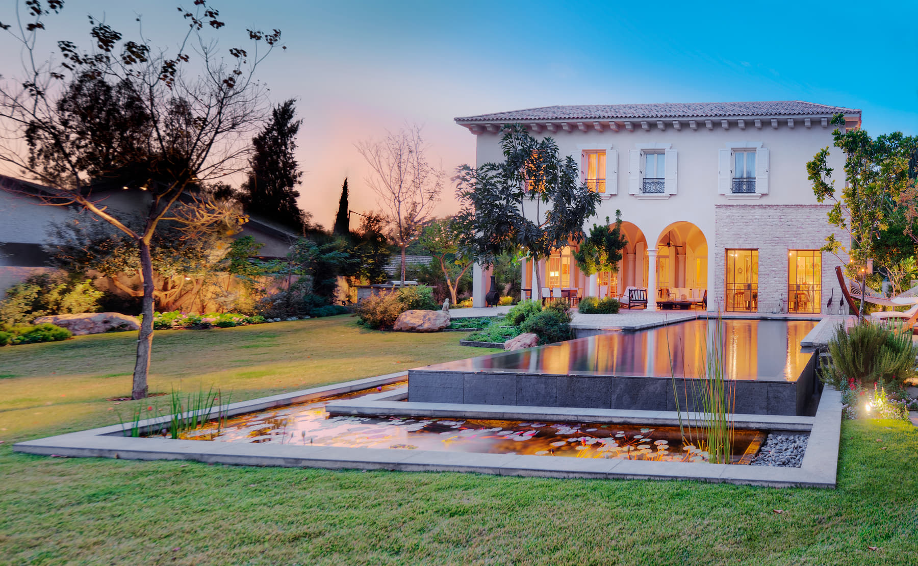 Elegant home reflected in a pool at dusk, interior lights glowing